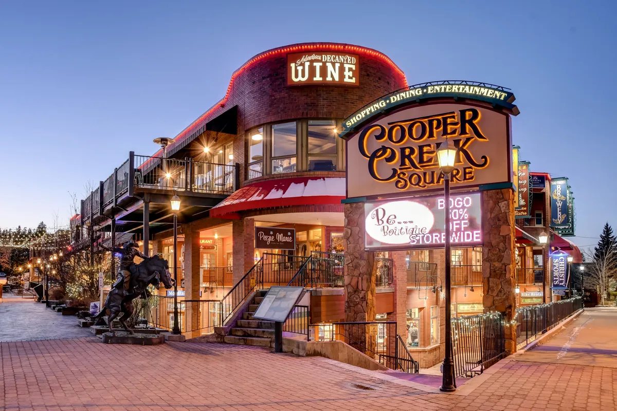 A vibrant exterior scene at Cooper Creek Square, highlighting outdoor seating, decorative lighting, and nearby shops—suggesting a lively local community and the opportunity for entertainment and exploration beyond the home.