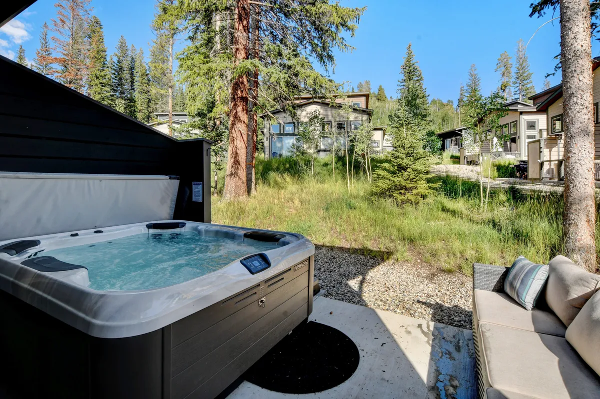 A serene outdoor area featuring a bubbling hot tub, comfortable seating, and lush greenery. The setup is inviting for socializing, unwinding after a day of adventure, or simply enjoying the natural surroundings.