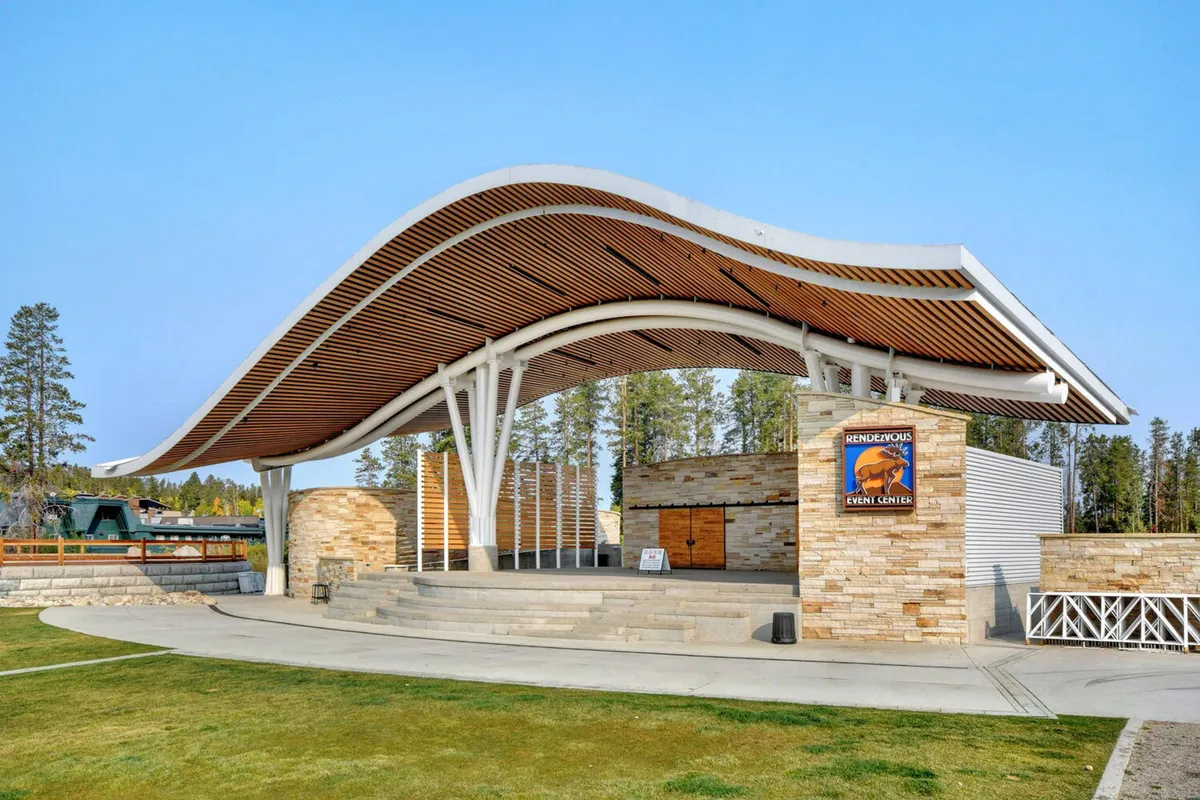 An exterior scene featuring a curved roof structure, stone walls, wooden accents, and event signage. This setting is used for outdoor concerts, community gatherings, and festivals—activities that reflect the vibrancy and opportunities available just beyond the home base.
