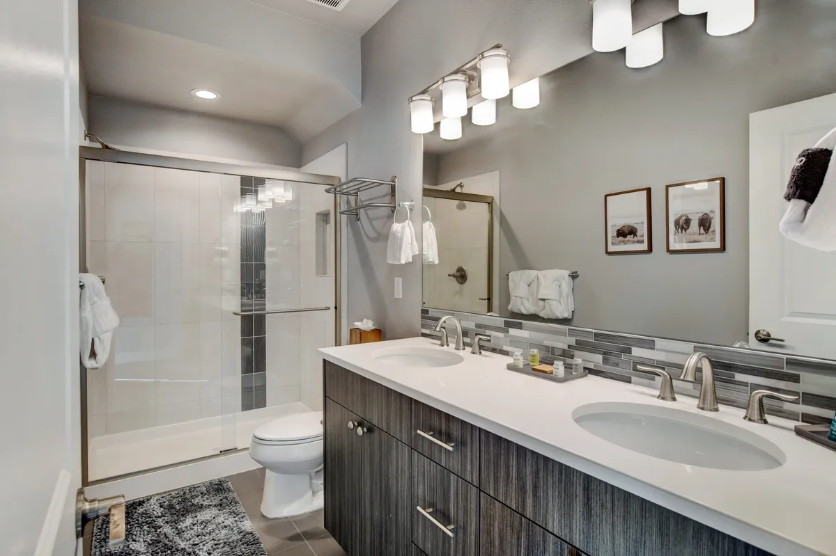 A modern bathroom showcasing a double sink vanity, glass shower enclosure, and framed wall art. The space exudes spa-like serenity, promising a comfortable and stylish setting for daily routines.