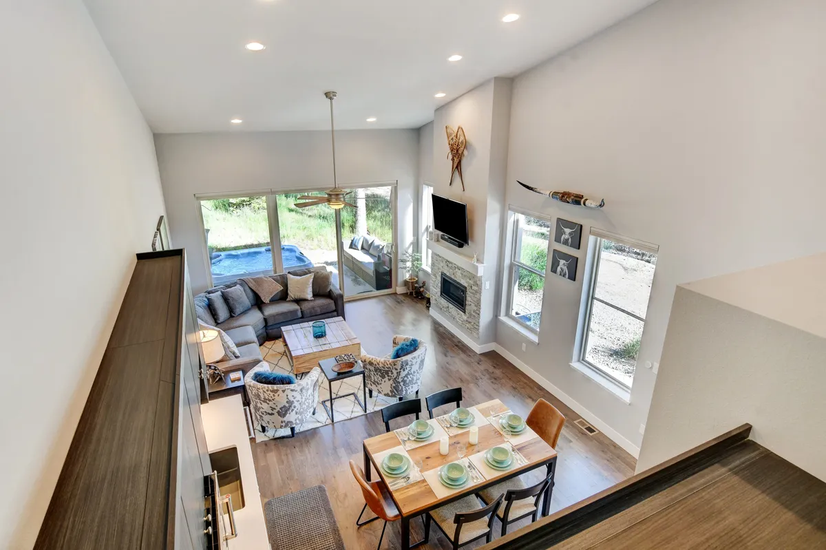 A welcoming living and dining area featuring a dining table set for a meal, a comfortable sofa, fireplace, and large sliding glass doors that open to the outdoors. Natural light pours in, and the view outside hints at close proximity to local attractions.