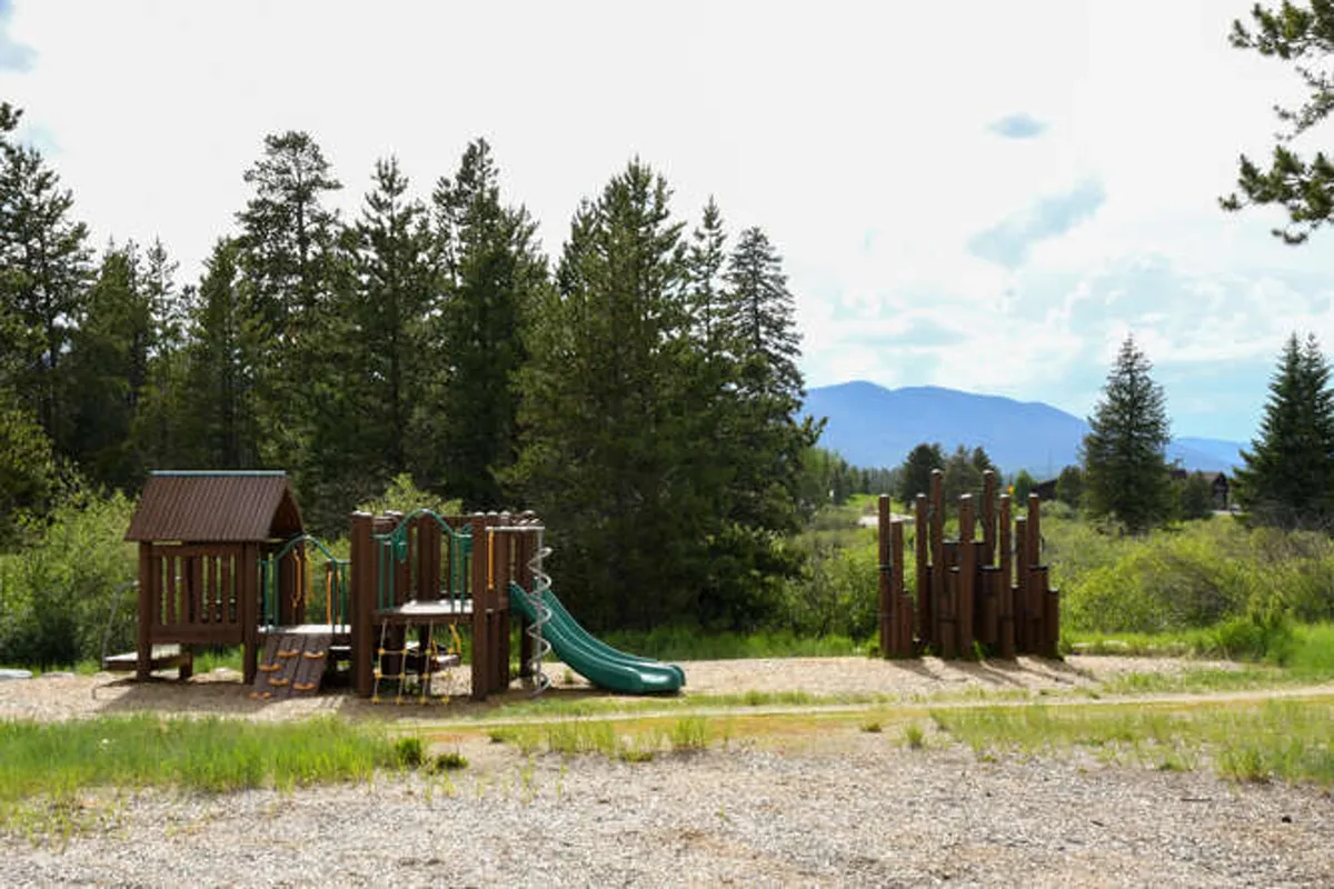 This image captures a cheerful playground set amidst tall trees, with children playing and families enjoying time together. The setting emphasizes direct access to outdoor recreation in a natural environment.