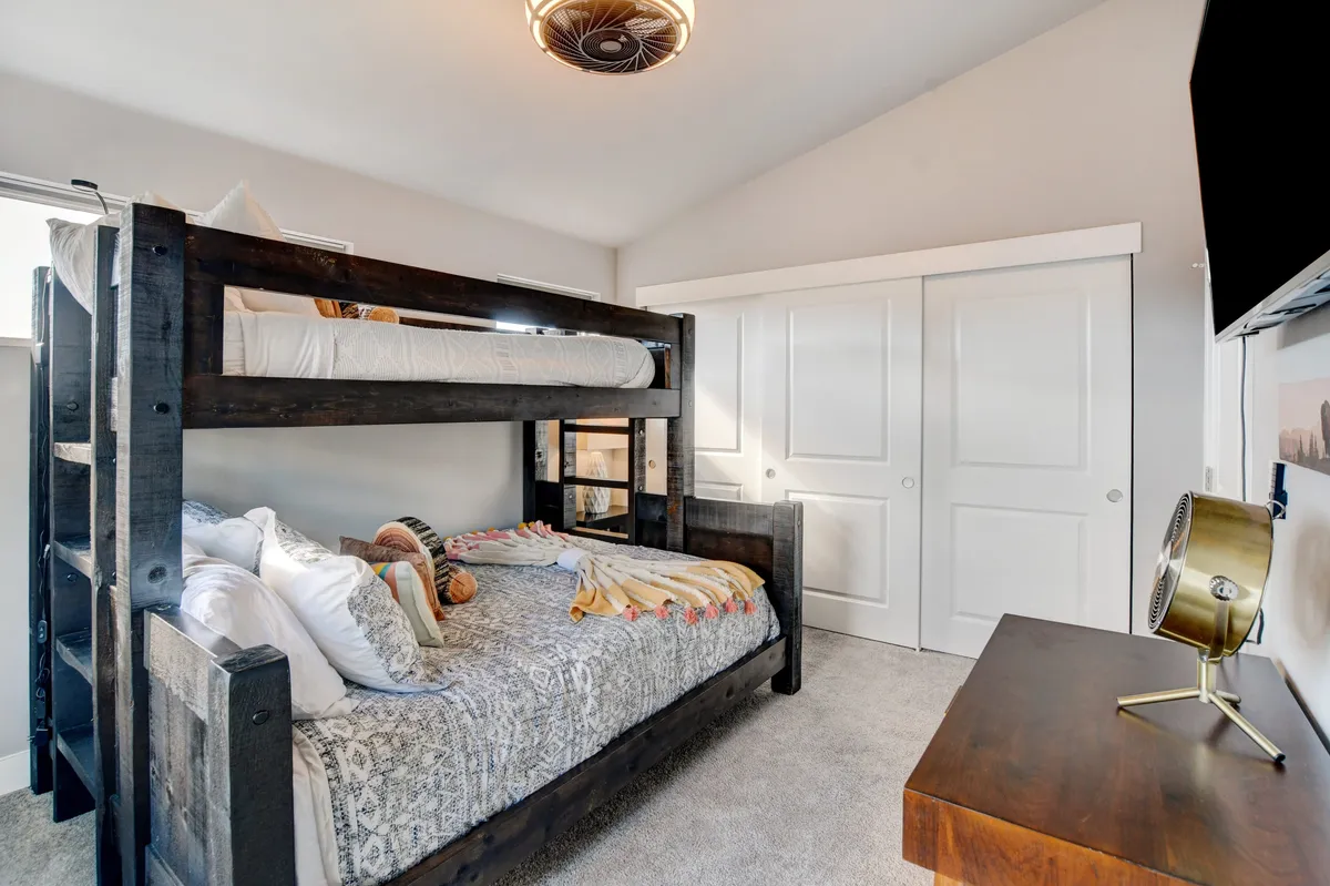 A playful and comfortable bedroom featuring a bunk bed with decorative pillows, fresh bed linens, and a desk with a lamp nearby. The room is designed for both rest and productivity, appealing to families or remote workers alike.