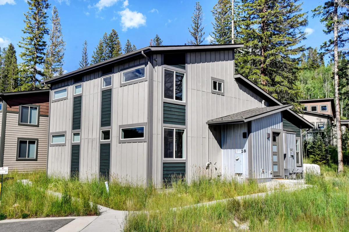 A modern mountain home stands amidst natural surroundings, with a landscaped front yard and inviting porch area. The exterior design is clean and welcoming, and the greenery around the home hints at nearby family-friendly outdoor adventures.