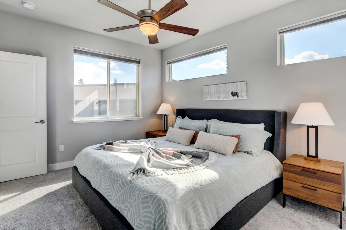 A serene bedroom with a large, inviting bed dressed in premium linens. The space features a ceiling fan above, nightstands on either side, and windows that let in soft natural light, creating a tranquil and restful atmosphere. The setup is ideal for relaxing after a busy day outdoors.