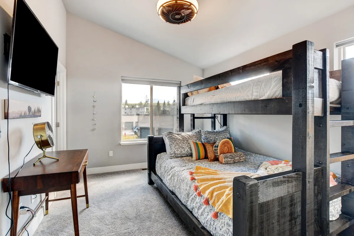 A playful and comfortable kids’ bedroom with a bunk bed, decorative pillows, and a wooden desk, radiating coziness and fun. The space looks perfect for relaxing, reading, and unwinding after a day of exploration.